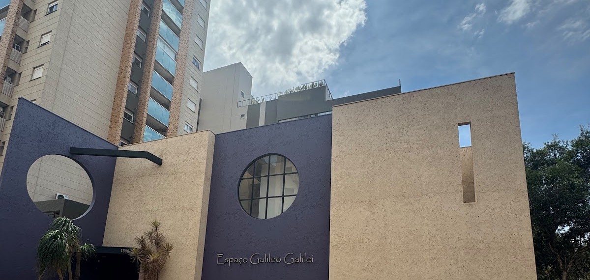 Fachada do Espaço Galileu Galilei: volumes de textura areia com planos violeta e duas janelas redondas